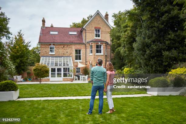 rear view of couple on grass looking at house - uk domestic garden stock pictures, royalty-free photos & images