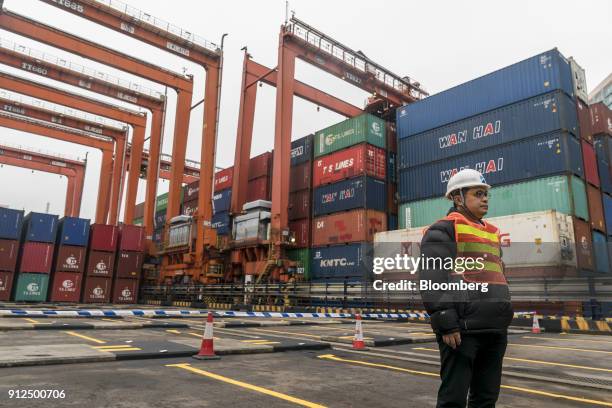 An employee stands near remote-controlled gantry cranes, left, and shipping containers in Container Terminal 9, operated by Hong Kong International...