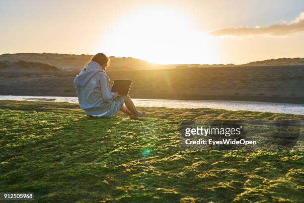 Woman sits alone on the rocks with colorful seaweed working with a notebook at the beach on January 19, 2018 in El Medano, Tenerife, Spain. Model...