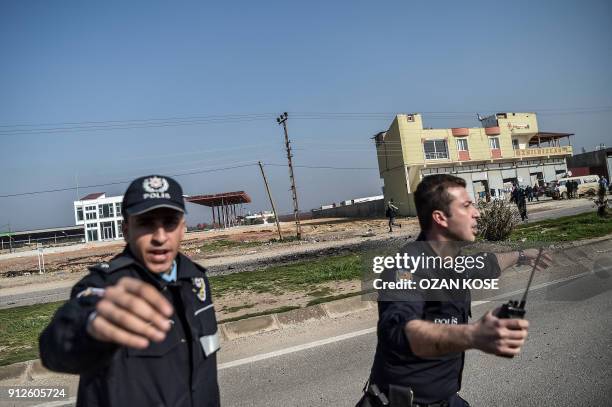 Turkish police officers work to push people back from the area after a rocket hit a road in the Reyhanli district in Hatay province, near the...