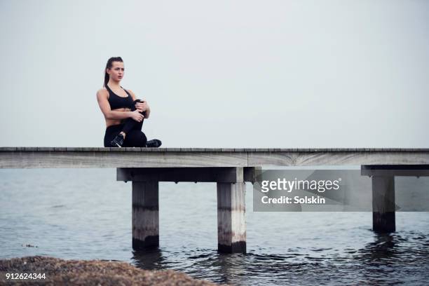 woman sitting on wooden pier, stretching after workout - flatten the curve 個照片及圖片檔
