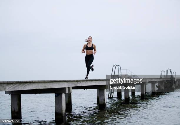 female athlete running on wooden pier - aplatir la courbe photos et images de collection