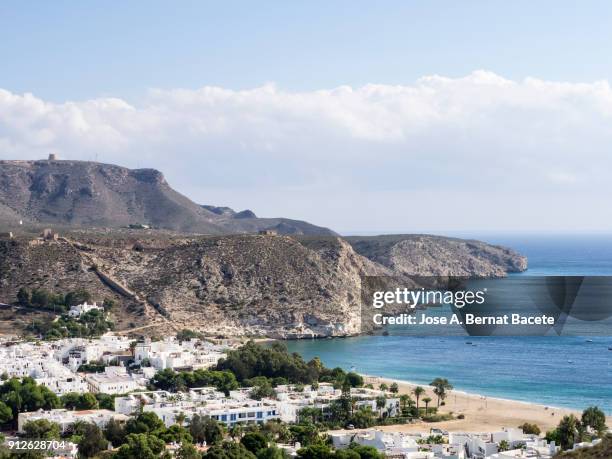 shore of the beach with waves and sand and the houses of a tourist town. cabo de gata - nijar natural park, beach of the port and town of san jose, biosphere reserve, almeria,  andalusia, spain. - biosphere planet earth stock pictures, royalty-free photos & images