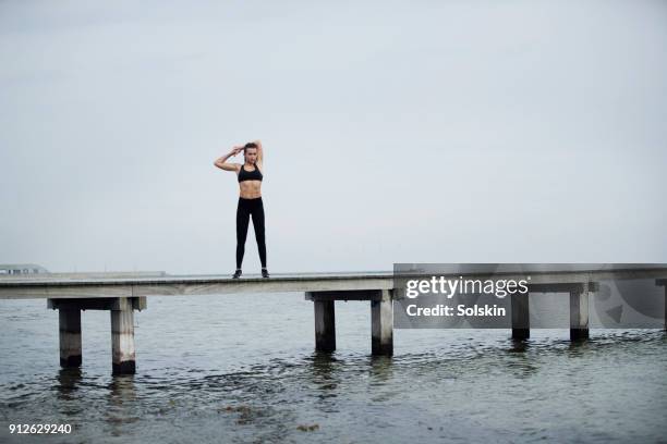 young woman stretching after exercise, standing on wooden pier - de curve afvlakken stockfoto's en -beelden