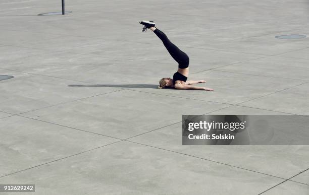 female athlete laying on concrete surface outdoors, stretching legs over head - achatar la curva de epidemia fotografías e imágenes de stock