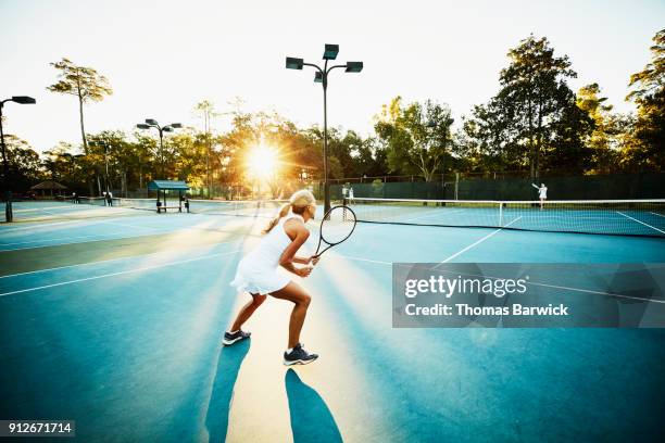 mature female tennis player preparing to return ball during early morning tennis match - atuendo de tenis fotografías e imágenes de stock