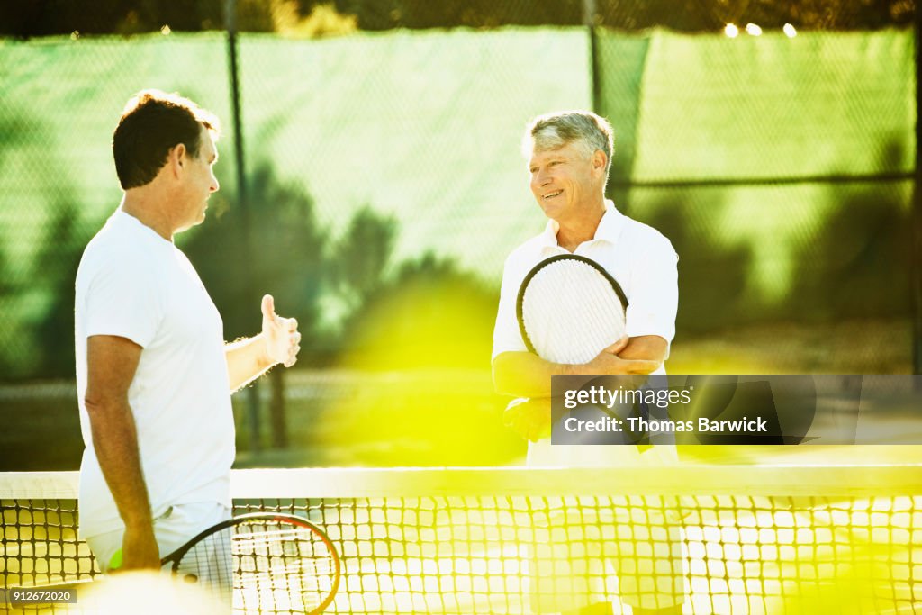 Two mature male tennis players in discussion at net after tennis match