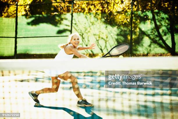 laughing mature female tennis player hitting backhand return at net during early morning tennis match - テニスネット ストックフォトと画像