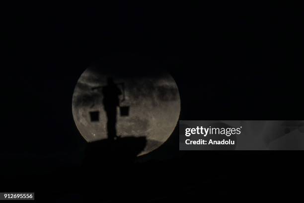 Silhouette of a man carrying baskets using shoulder pole is seen in front of the 'Super blue blood moon' in Gevas district of Van province of Turkey...
