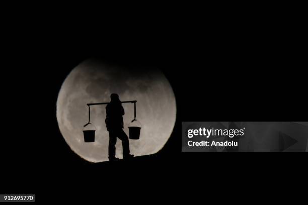 Silhouette of a man carrying baskets using shoulder pole is seen in front of the 'Super blue blood moon' in Gevas district of Van province of Turkey...