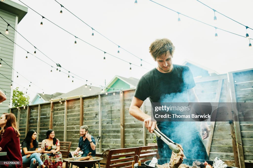 Man grilling steaks for friends at backyard barbecue during party