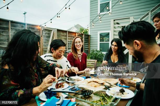 smiling and laughing friends sharing dinner at table in backyard - inviter photos et images de collection