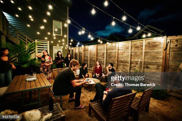 friends sitting around fire during neighborhood backyard party on summer evening - dinner party stock pictures, royalty-free photos & images