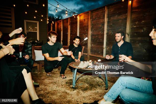 group of friends roasting marshmallows over fire in backyard on summer evening - hot latin nights stock pictures, royalty-free photos & images