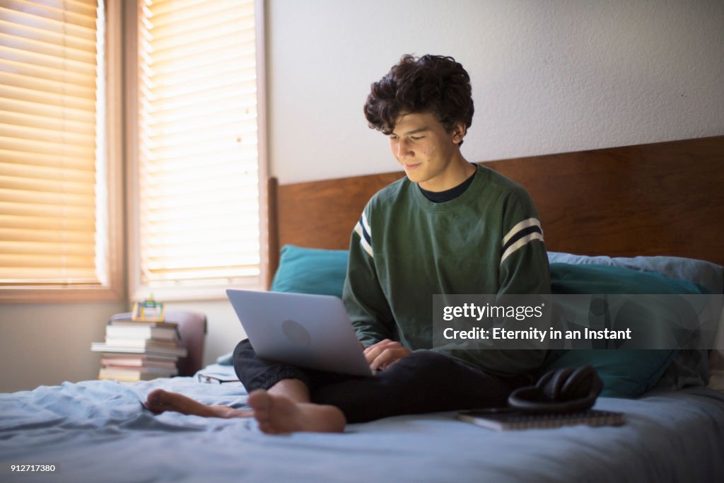 Teenage boy using his laptop in his bedroom