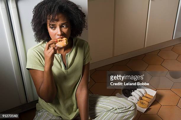 woman seated on kitchen floor at night eating doug - vreten stockfoto's en -beelden