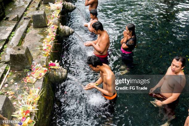 group of people showering under the waterspouts at the tirta empul temple in bali, indonesia - tirta empul temple stock pictures, royalty-free photos & images