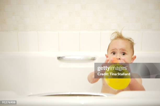 Month Ella-Mai Horswill-Rydquist looks up startled, as she plays with a rubber duck in the bath.
