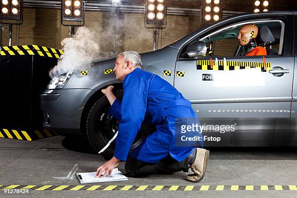 a technician examining a smoking crash test car wi - crash test dummy stockfoto's en -beelden