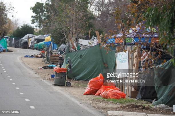 Orange trash bags sit outside tents and tarps of a homeless encampment along the Santa Ana riverbed bicycle path near Angel Stadium in Anaheim,...