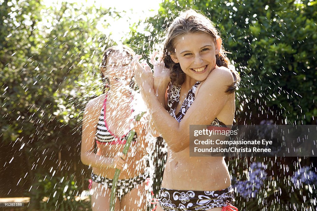 Two girls in bathing suits playing with water hose