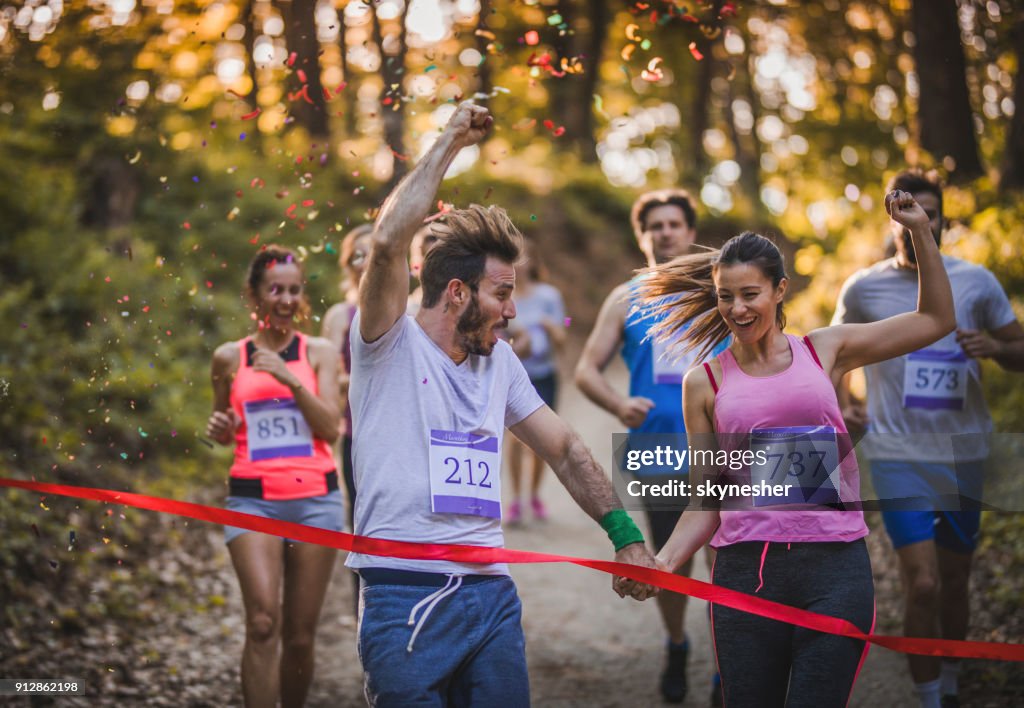Happy athletic couple holding hands while running through finish line together.