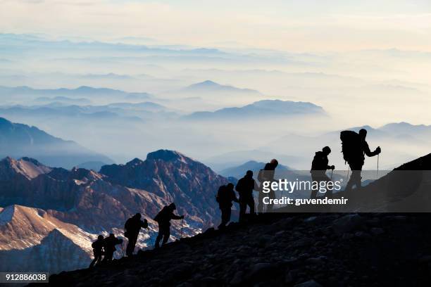 silhouetten van wandelaars at dusk - team climbing up to mountain top stockfoto's en -beelden