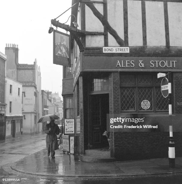 Men passes by William The Fourth, Public House, Bond Street, on a rainy day, London, UK, circa 1960.