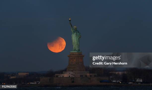 The super blue blood moon is partially eclipsed as it sets beside the Statue of Liberty on January 31, 2018 in New York City.