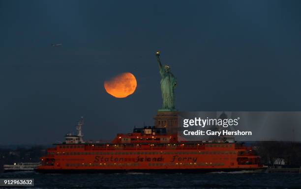The super blue blood moon is partially eclipsed as it sets beside the Statue of Liberty on January 31, 2018 in New York City.