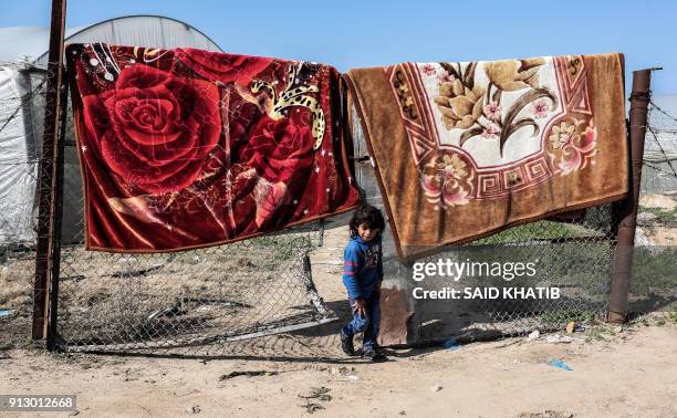 Palestinian child walks through a fence between two blanks hung out in the sun, in the Rafah refugee camp in the southern Gaza Strip on February 1,...