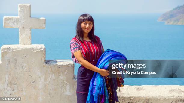 young mayan woman carrying woven patterned tablecloths for sale at shore of lake atitlan guatemala - guatemala stock pictures, royalty-free photos & images