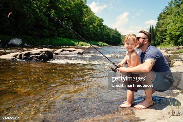 Millennial father showing son how to fish in a river in summer nature.