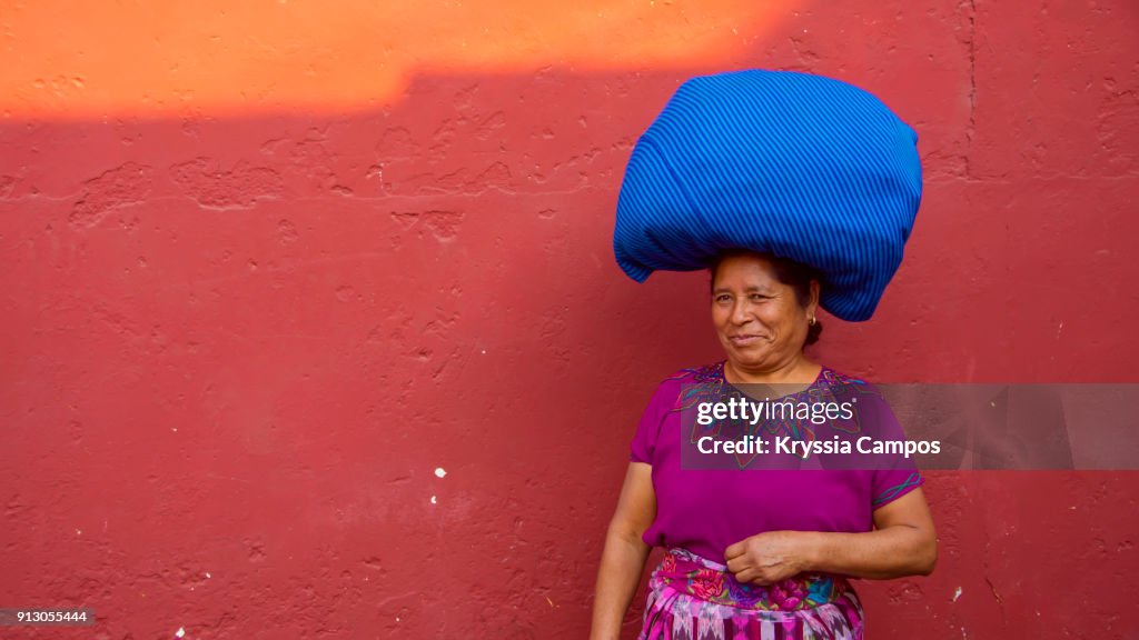 Senior mayan woman in typical costume with bundles balanced on her head. Antigua - Guatemala.