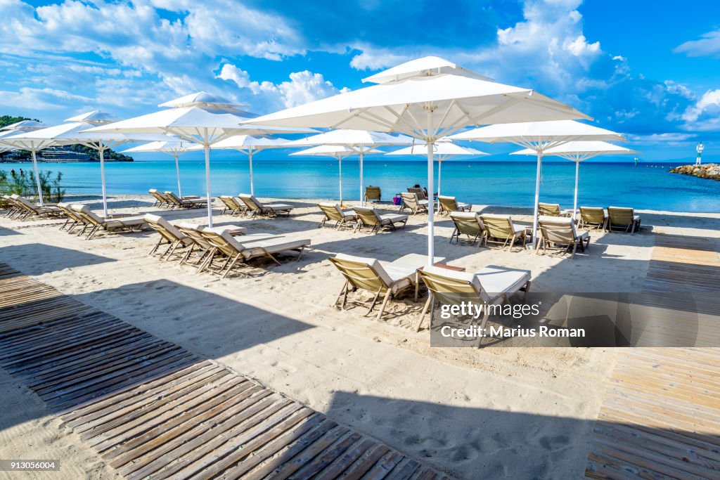 White lounge chairs and parasols on sandy Sani beach, with beautiful blue sea and clody sky, Kassandra, Greece.