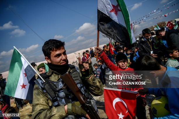 Turkish-backed Syrian rebel fighter gestures as he holds Free Syrian Army flag next to Syrian children holding Turkish national flag and a Free...