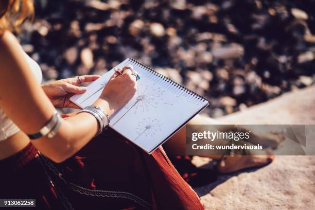 bohemian woman sketching nature sitting on rock at the beach - silver bracelet stock pictures, royalty-free photos & images