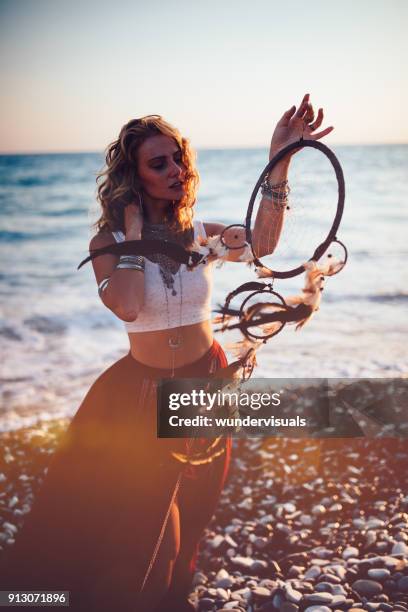hippie woman holding dreamcatcher at the beach at sunset - bobo tribe stock pictures, royalty-free photos & images