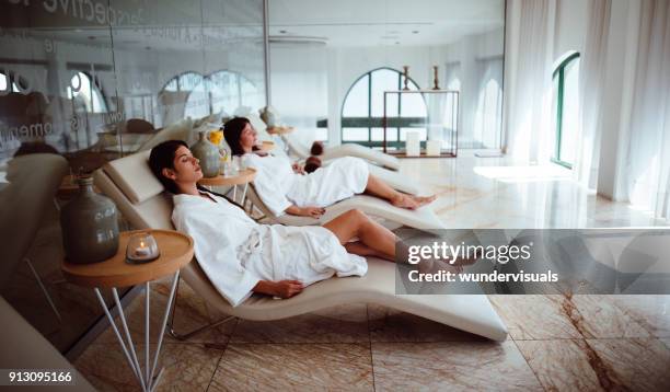 mujeres jóvenes en mantos blancos relajantes en el centro de spa de belleza - masaje fotografías e imágenes de stock