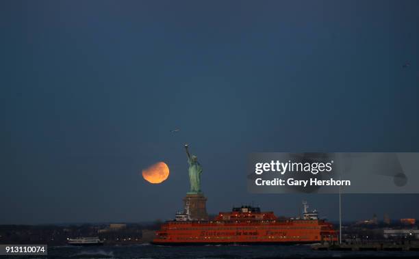 The eclipsed super blue blood moon sets next to the Statue of Liberty at sunrise on January 30, 2018 in New York City.