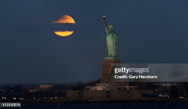 The eclipsed super blue blood moon passes through a cloud as it sets next to the Statue of Liberty at sunsrise on January 30, 2018 in New York City.