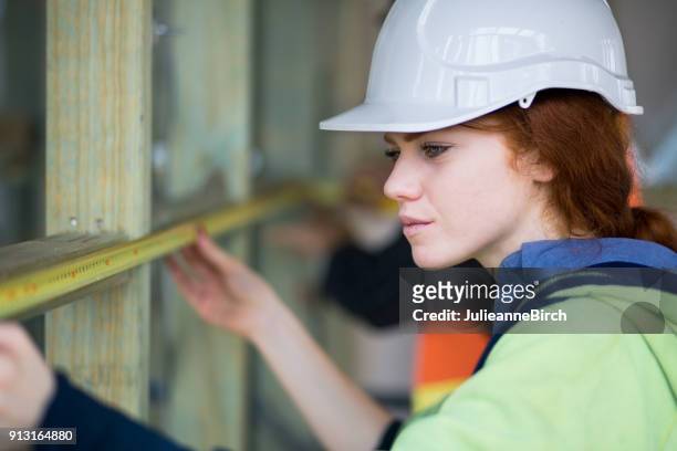young woman carpenter on building site measuring with tape measure - builder apprenticeship stock pictures, royalty-free photos & images