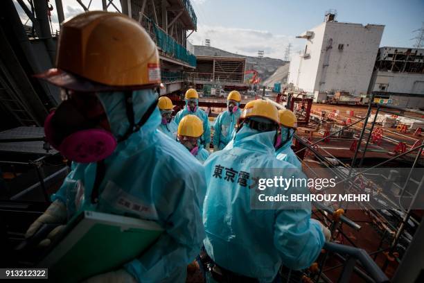 In this picture taken on January 31, 2018 employees of Tokyo Electric Power Company stand in front of the company's reactor number 3 at Fukushima...