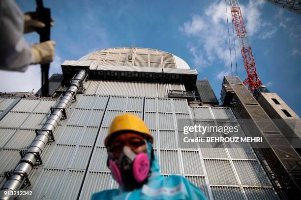 In this picture taken on January 31, 2018 an employee of Tokyo Electric Power Company stands in front of the company's reactor number 3 at Fukushima...