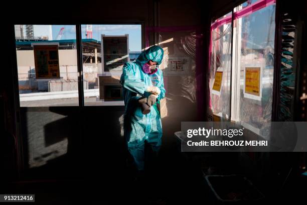 In this picture taken on January 31, 2018 an employee of Tokyo Electric Power Company takes off his gloves as he holds a geiger counter to measure...