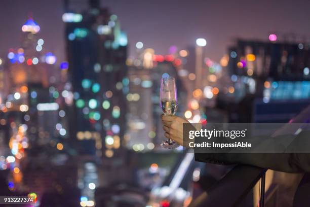 one man's hand is holding a glass wine with the bokeh of city lights in the background - impossiable fotografías e imágenes de stock