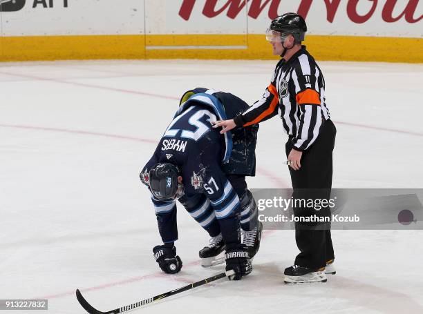 Referee Kelly Sutherland lends a hand to Tyler Myers of the Winnipeg Jets as he struggles off the ice after blocking a shot during third period...