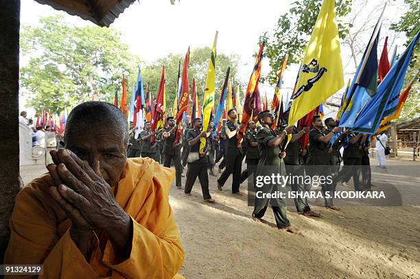 Buddhist monk gestures as Sri Lankan soldiers hold aloft regimental flags as they take part in a Buddhist ceremony where the military offered flags...