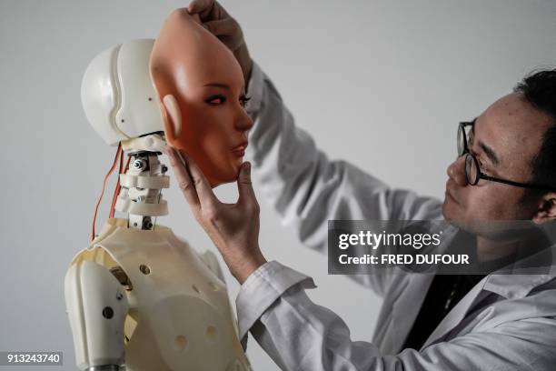 This photo taken on February 1, 2018 shows an engineer holding a silicon face against the head of a robot at a lab of a doll factory of EXDOLL, a...