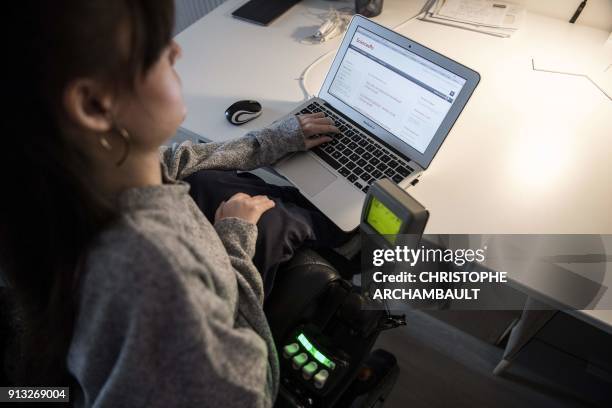 Disabled woman wroks on her computer in her wheelchair at her flat in Paris on January 18, 2018. / AFP PHOTO / CHRISTOPHE ARCHAMBAULT